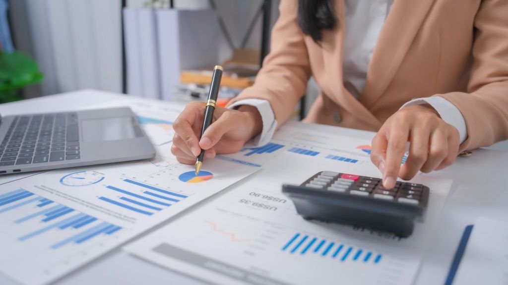 A bookkeeper reviews financial information and does some calculations on a calculator.