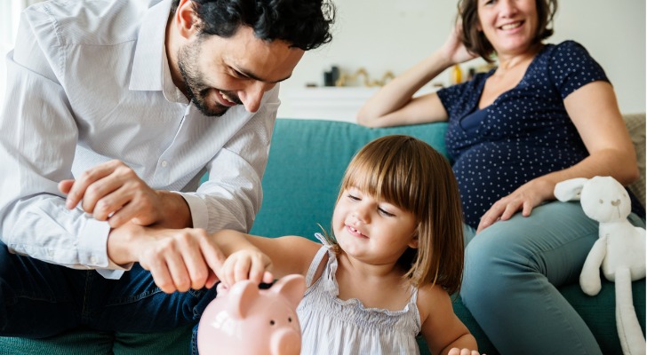 A father teaching a daughter how to save money with a piggy bank.
